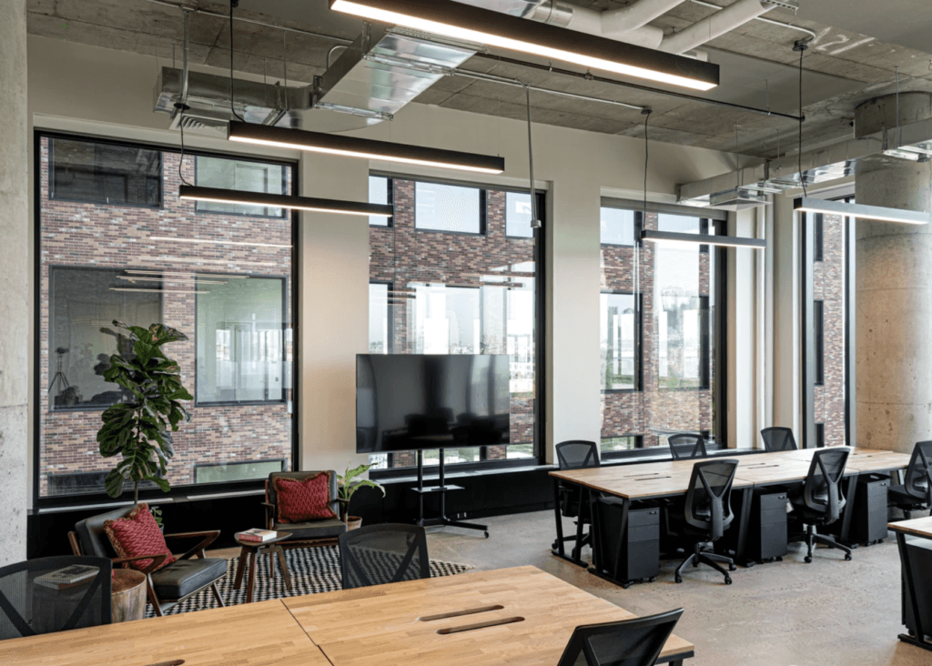 Industrial-style coworking space with wooden desks, large windows, and modern exposed ceilings