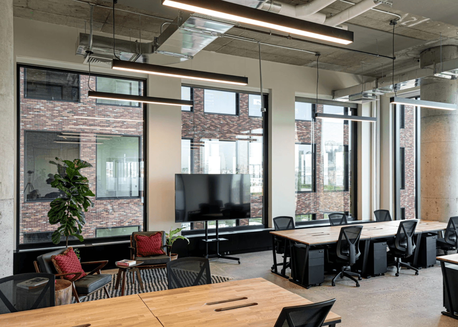 Industrial-style coworking space with wooden desks, large windows, and modern exposed ceilings