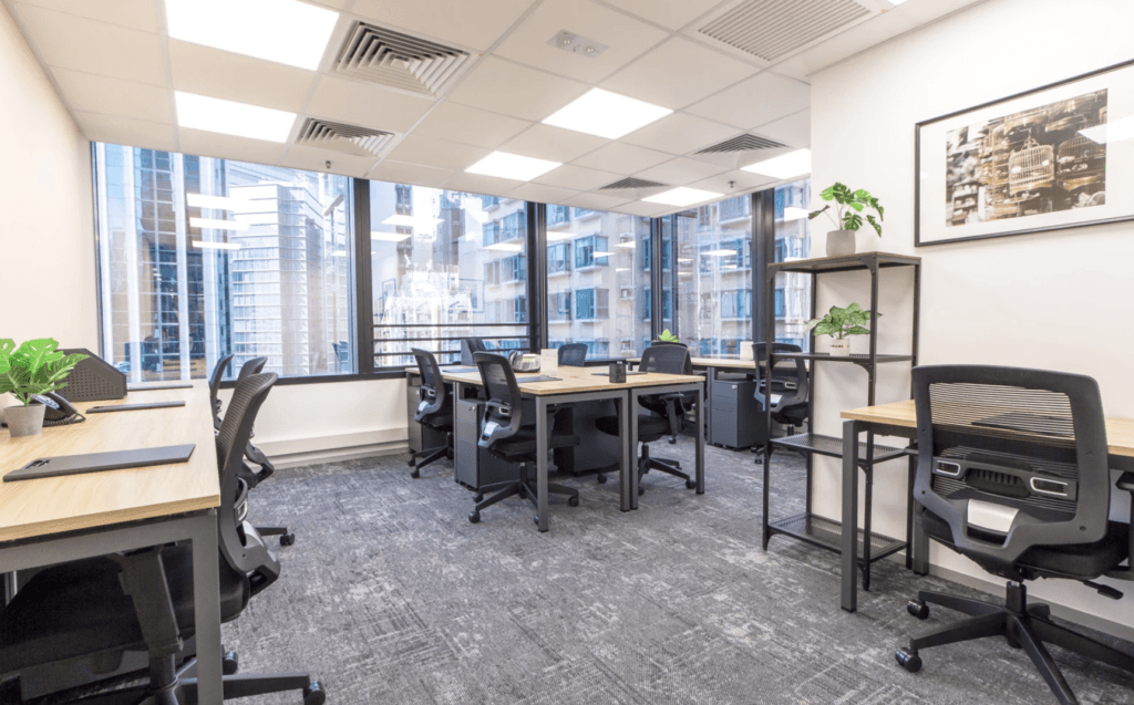 Modern office with multiple desks, ergonomic chairs, large windows, and city views in the background.