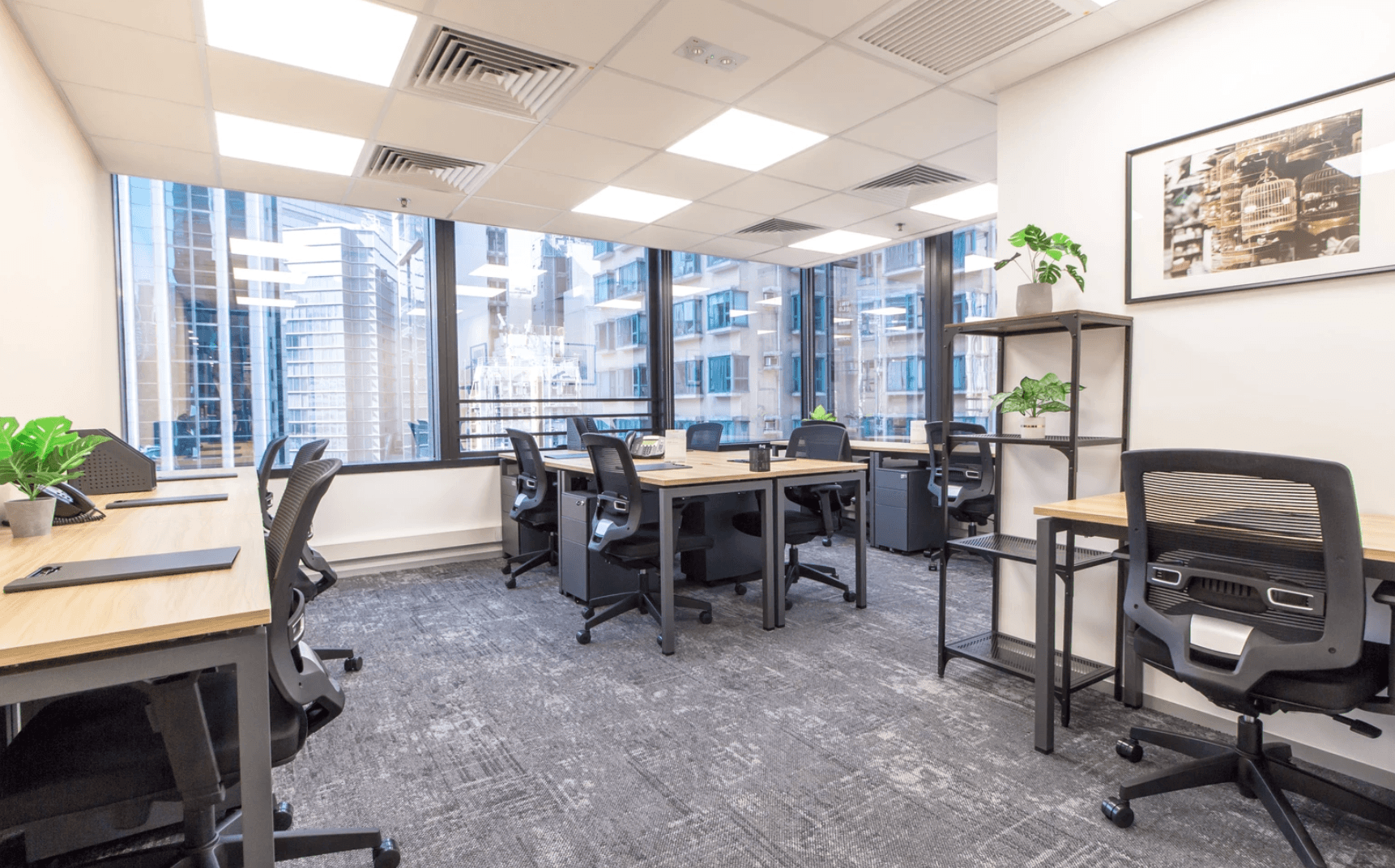 Modern office with multiple desks, ergonomic chairs, large windows, and city views in the background.