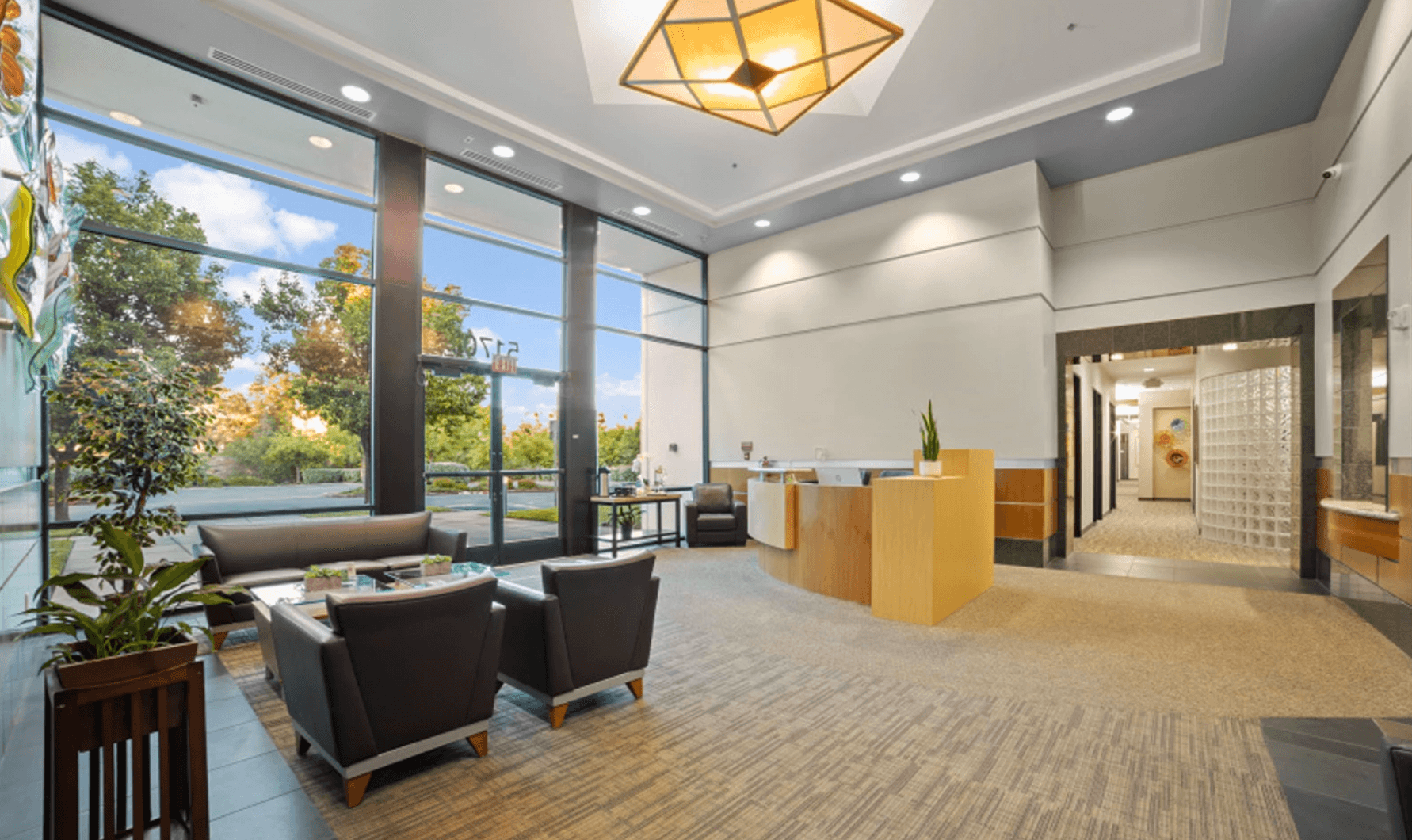 Bright office lobby with large glass windows, modern furniture, and a wooden reception desk.